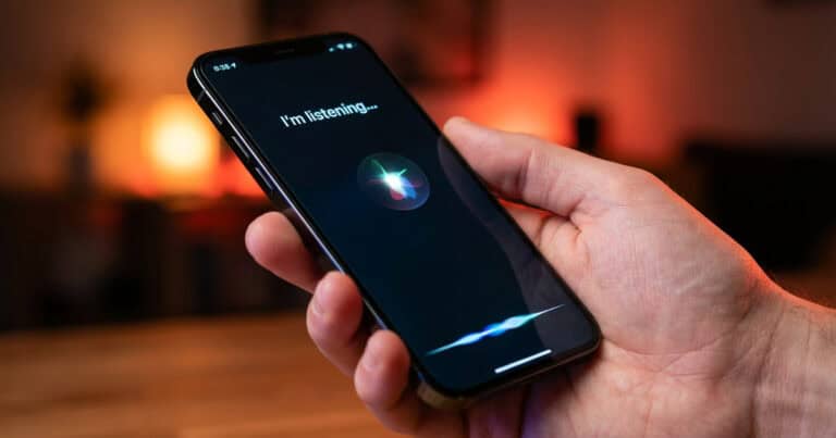 A person holding an iPhone displaying Siri listening mode with the text “I’m listening…” on the screen.